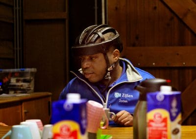 Man met helm op drinkt koffie. Op tafel staan mokjes en koffiemelk