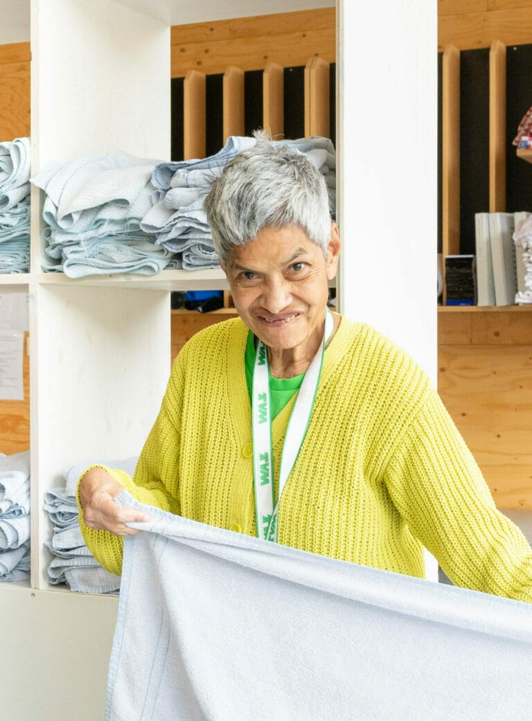 Vrouw in geel vest vouwt een witte handdoek op